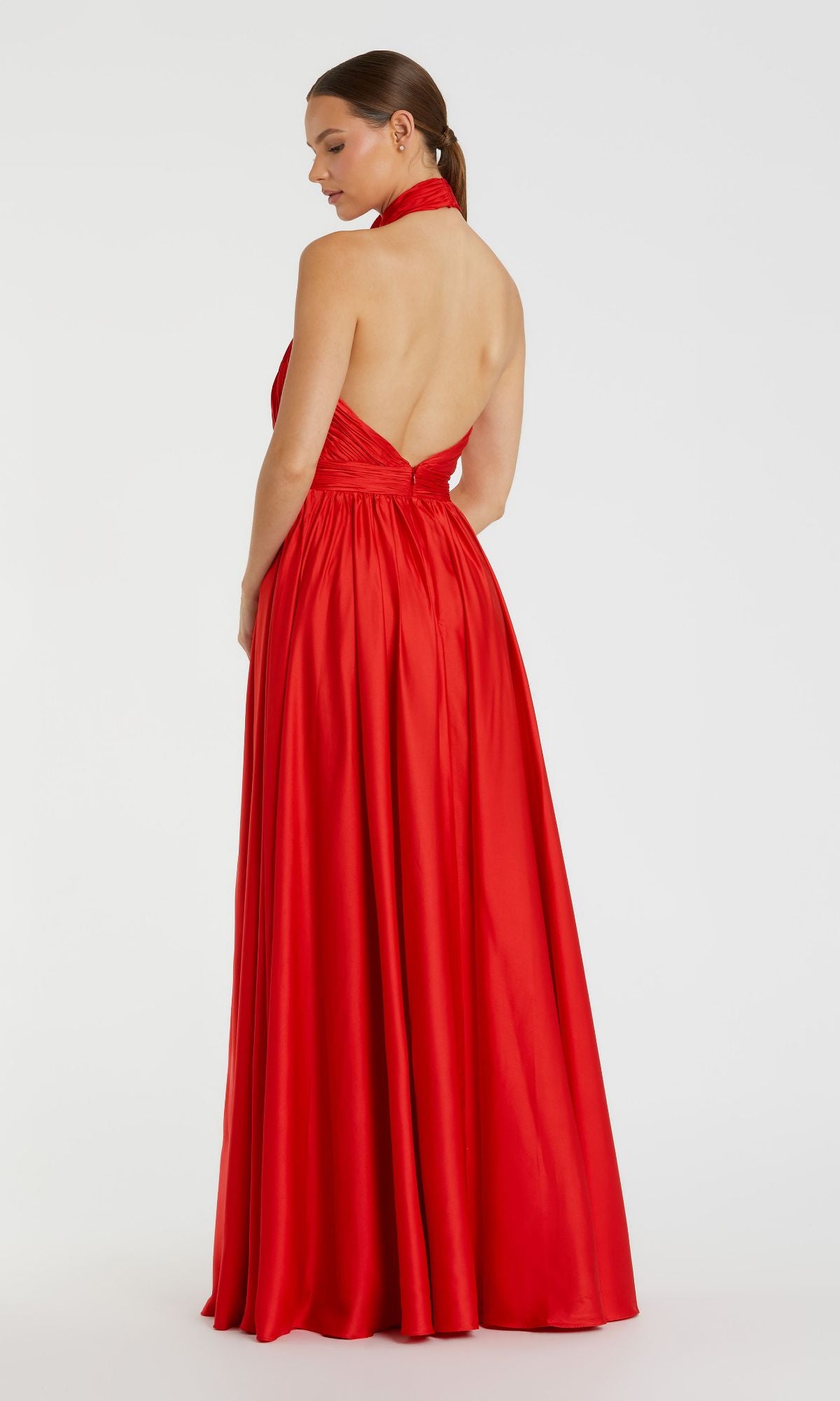 A woman faces away, modeling the Mac Duggal 49333 High-Neck Halter Formal Dress—a floor-length red gown with an open back, fitted bodice, and flowing skirt—set against a plain white background.